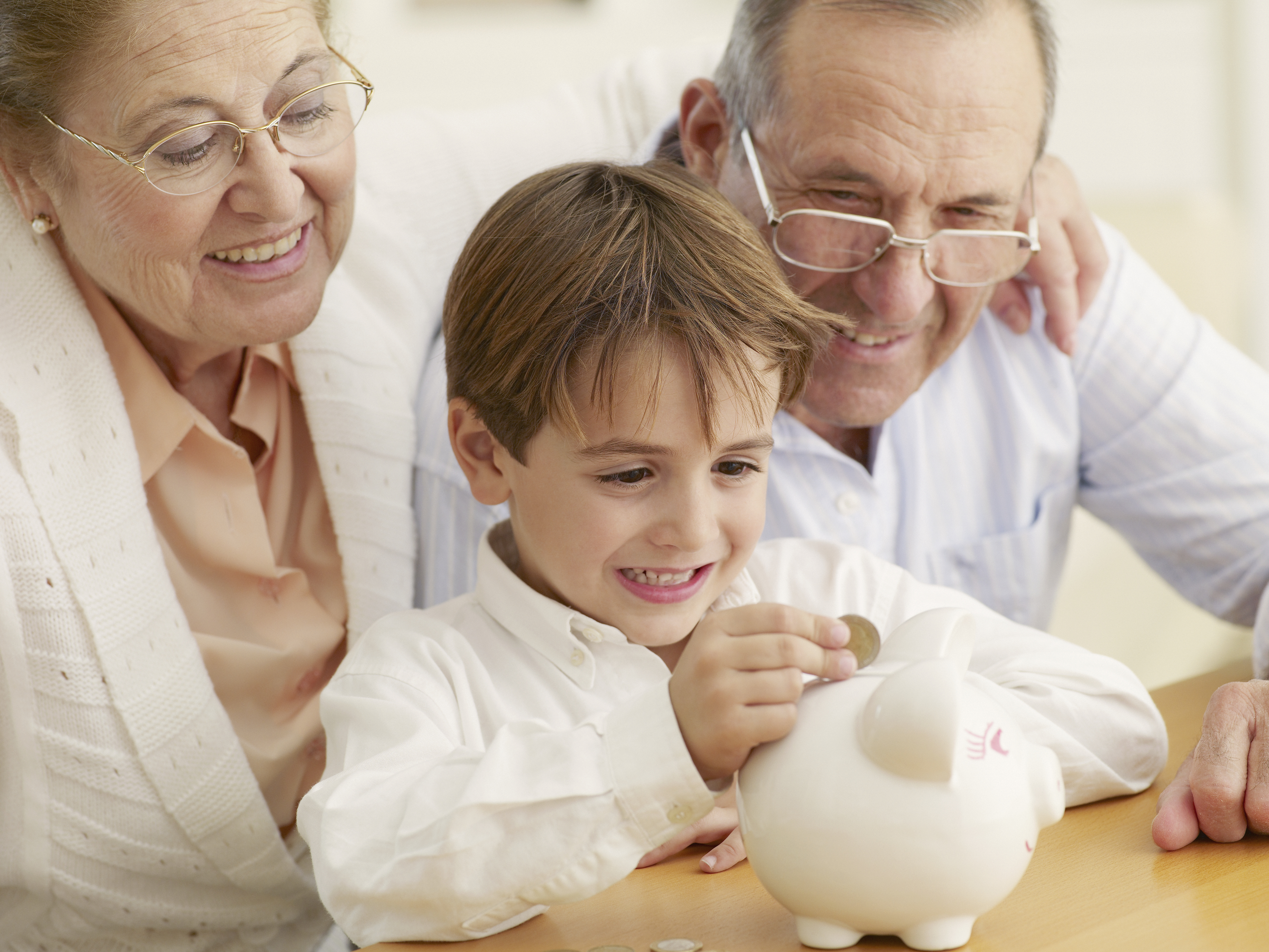 an elderly couple with presumably their grandchild who is putting a coin in a piggy bank